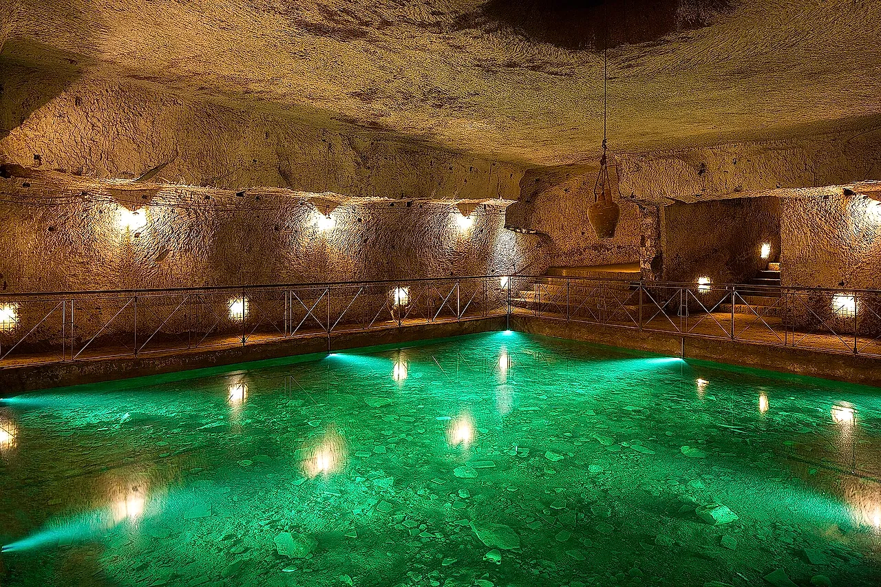 A Renaissance cistern with softly lit green water in the Galleria Borbonica, Naples