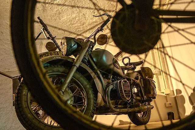 A 1940s motorcycle on display behind a spoked wheel in the Galleria Borbonica, Naples