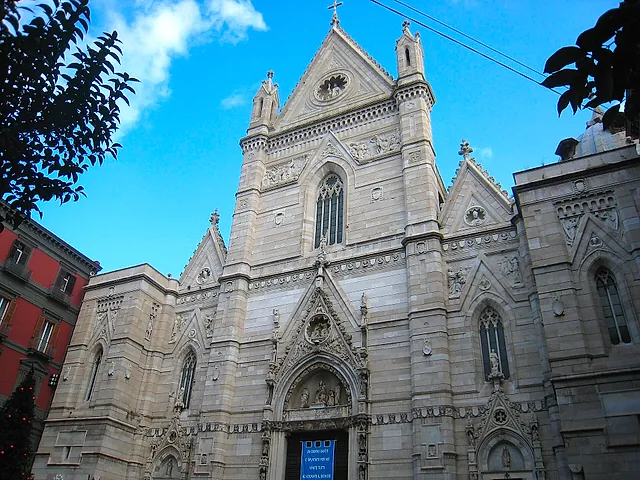 The Gothic-style façade of Naples Cathedral against a blue sky